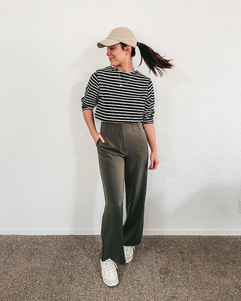 Black and white striped long-sleeve top with olive wide-leg trousers, beige cap, and white sneakers