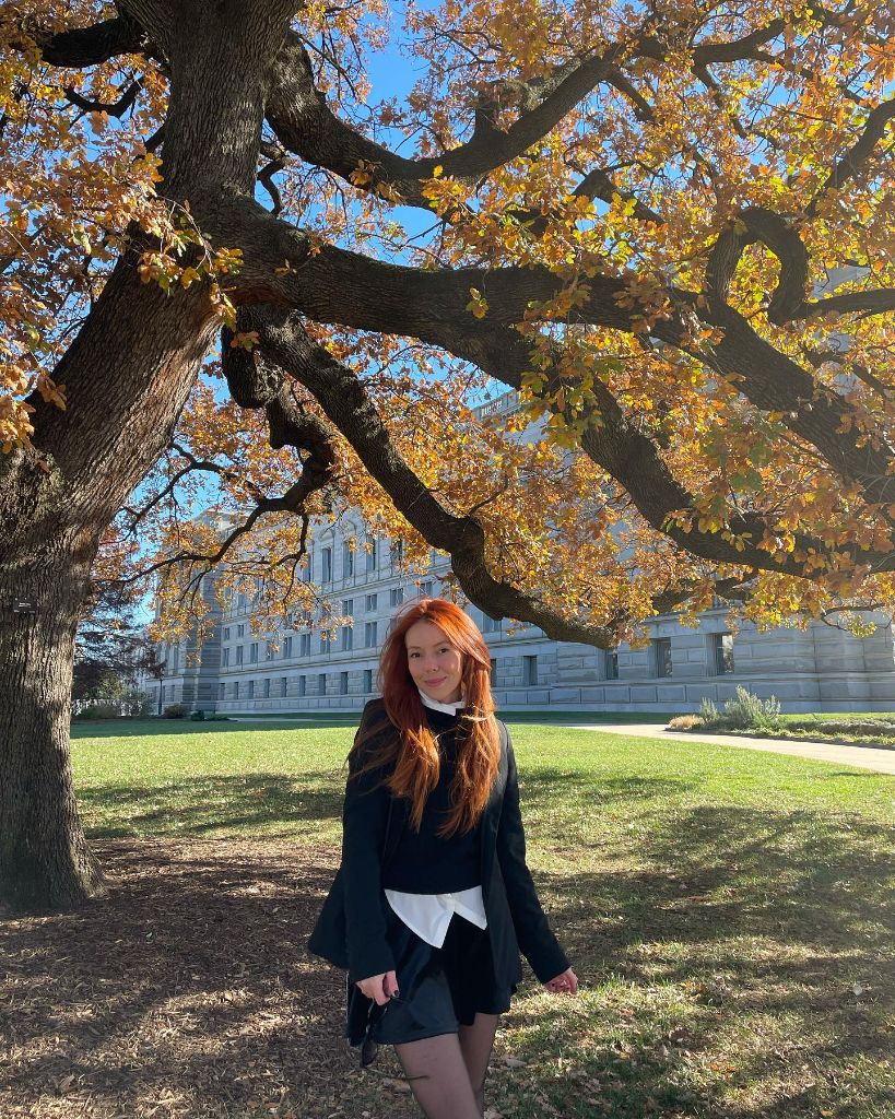 Black cropped jacket over white collared shirt with black mini skirt, autumn park setting