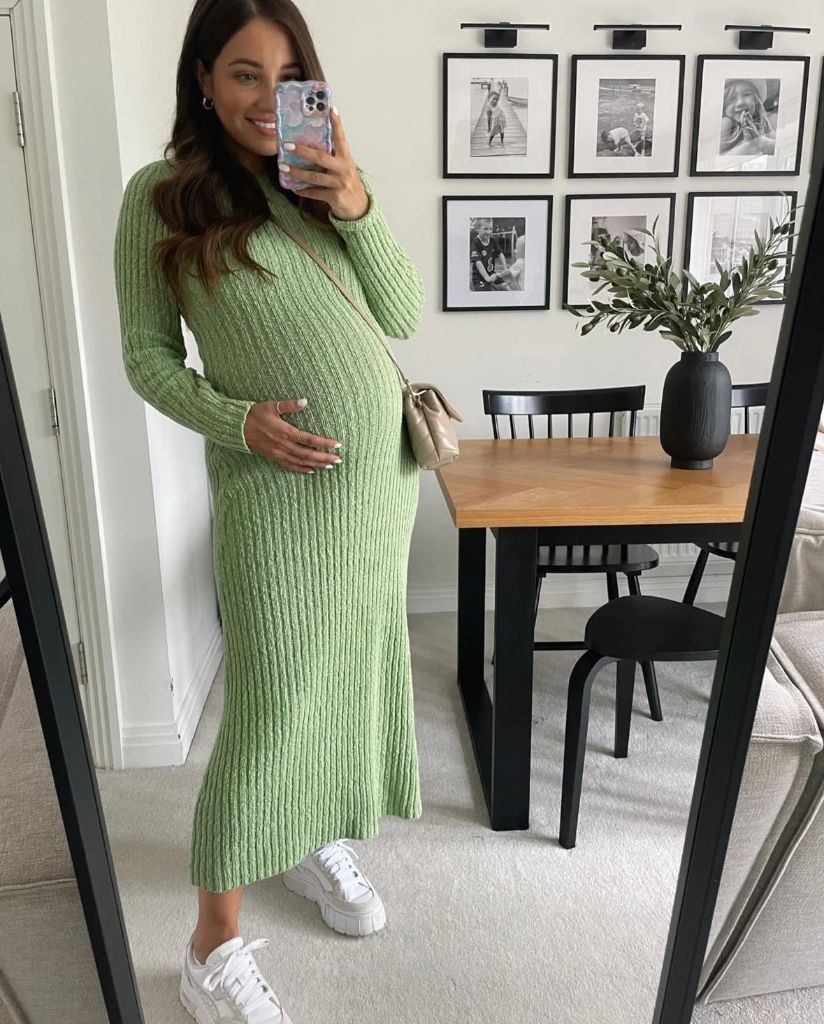 Mirror selfie of pregnant woman in green ribbed knit midi dress with white sneakers and crossbody bag