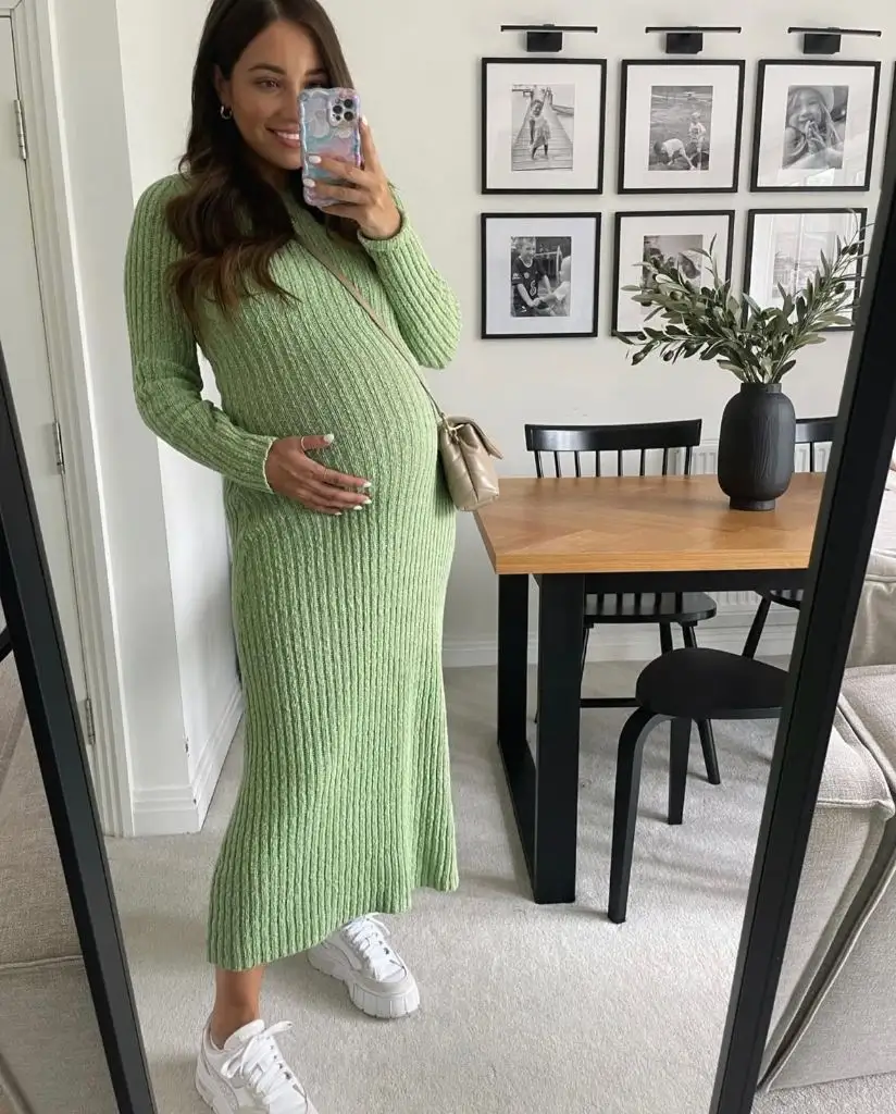 Mirror selfie of pregnant woman in green ribbed knit midi dress with white sneakers and crossbody bag
