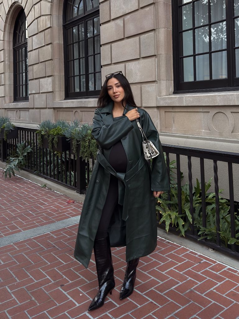 Pregnant woman in dark green leather trench coat, black bodycon outfit, croc boots, and snakeskin bag