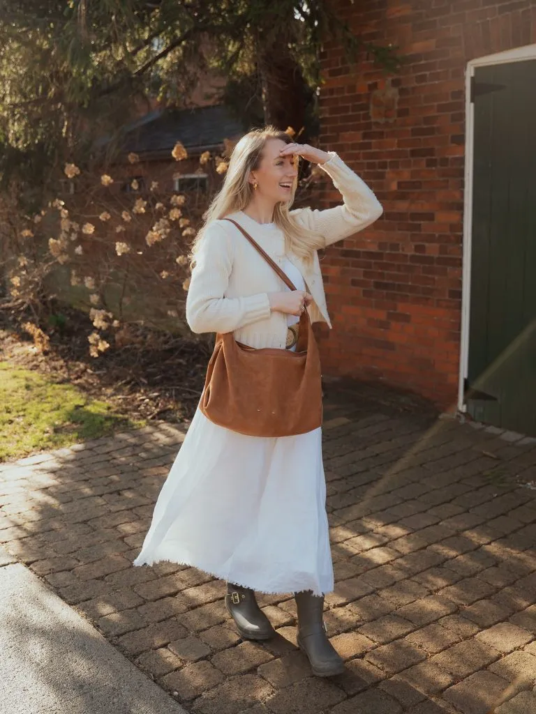 Woman in white dress with brown bag standing on brick path