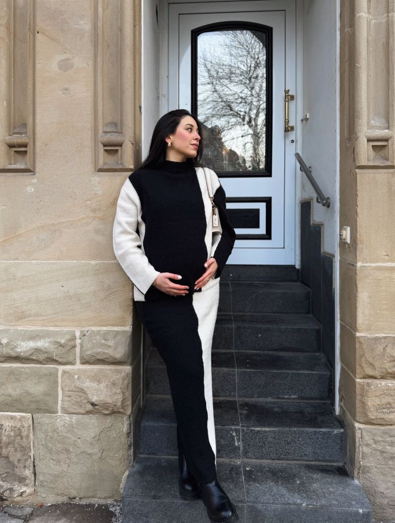 Pregnant woman in black and cream color-block knit sweater and pants with boots
