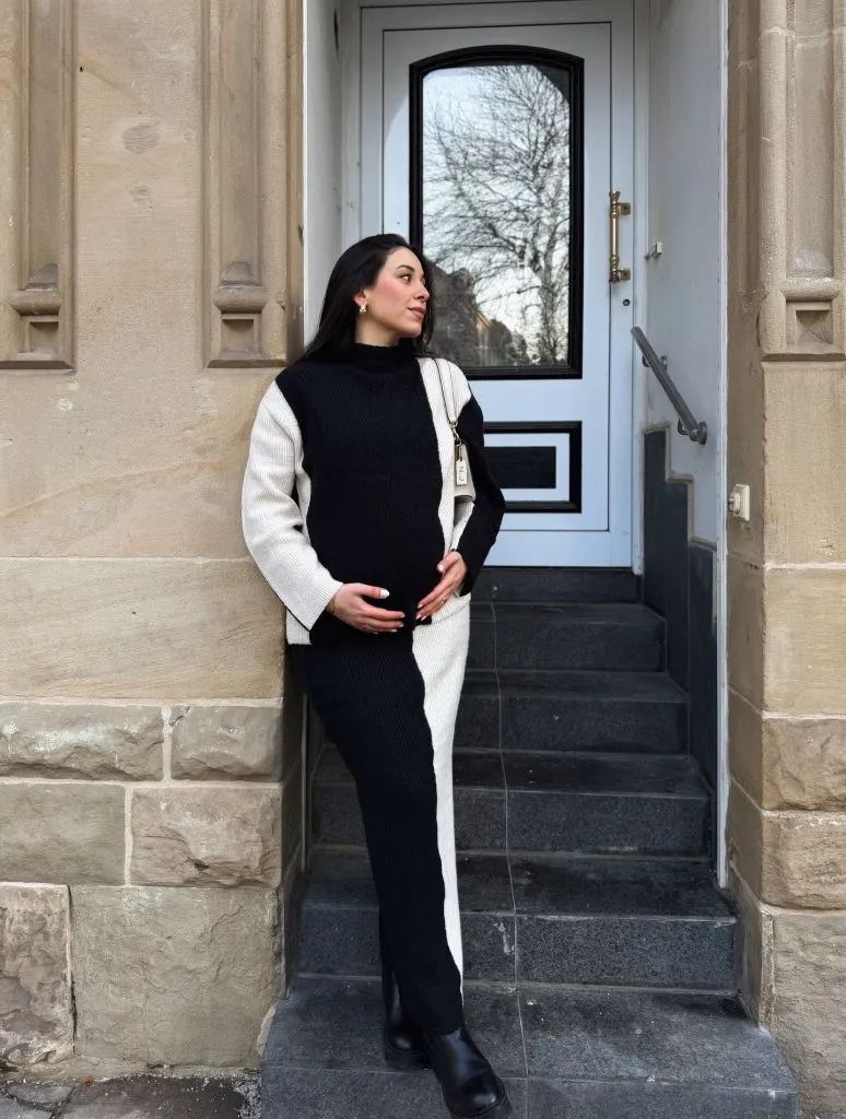 Pregnant woman in black and cream color-block knit sweater and pants with boots