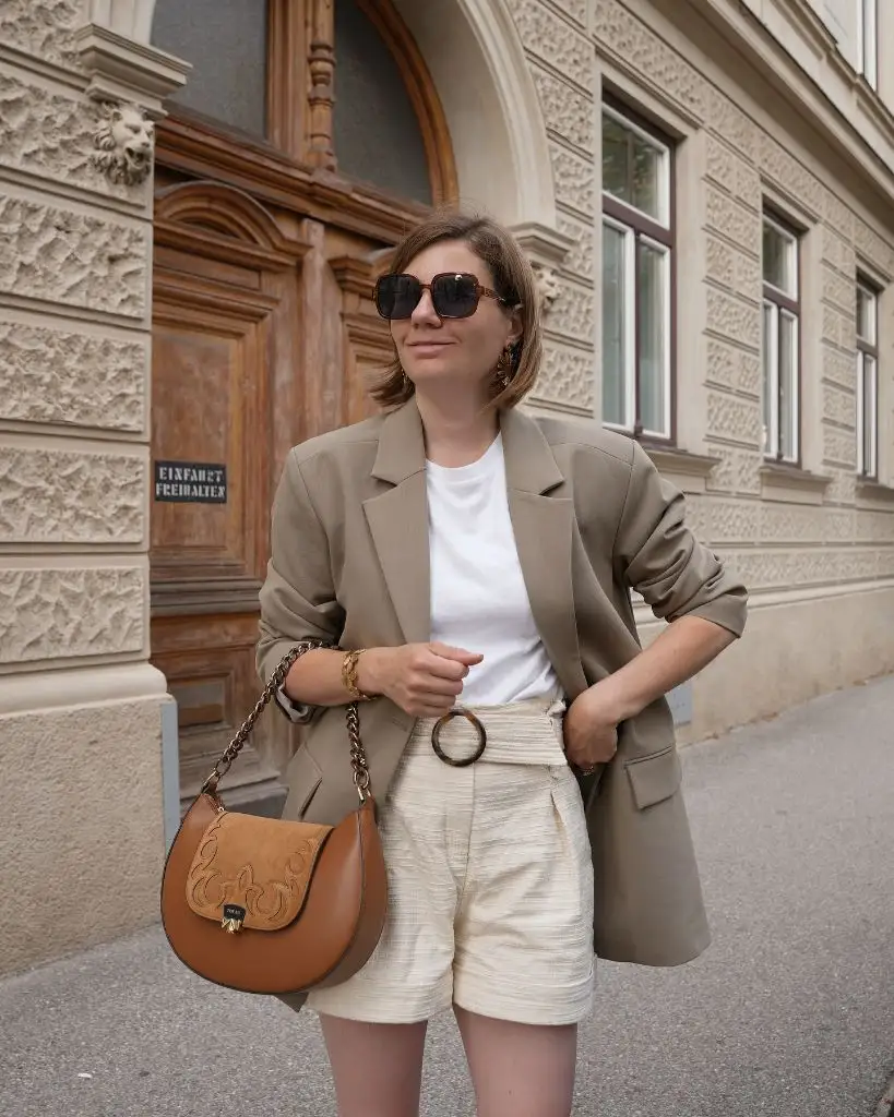 Olive blazer over white tee with cream textured shorts, tan saddle bag, and gold jewelry