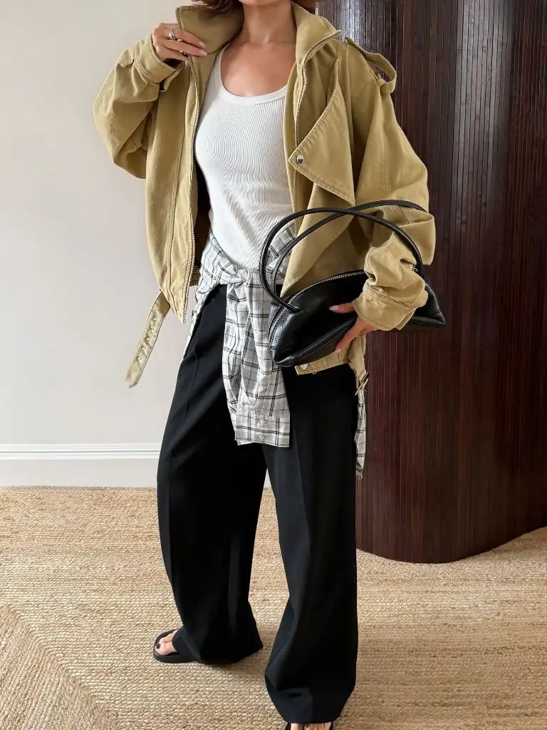 Khaki oversized parka jacket layered over white tank with plaid shirt and black wide pants