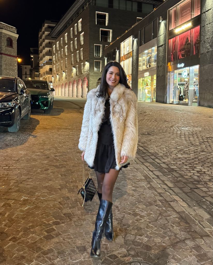 Fur coat with black mini dress and tall boots on cobblestone street