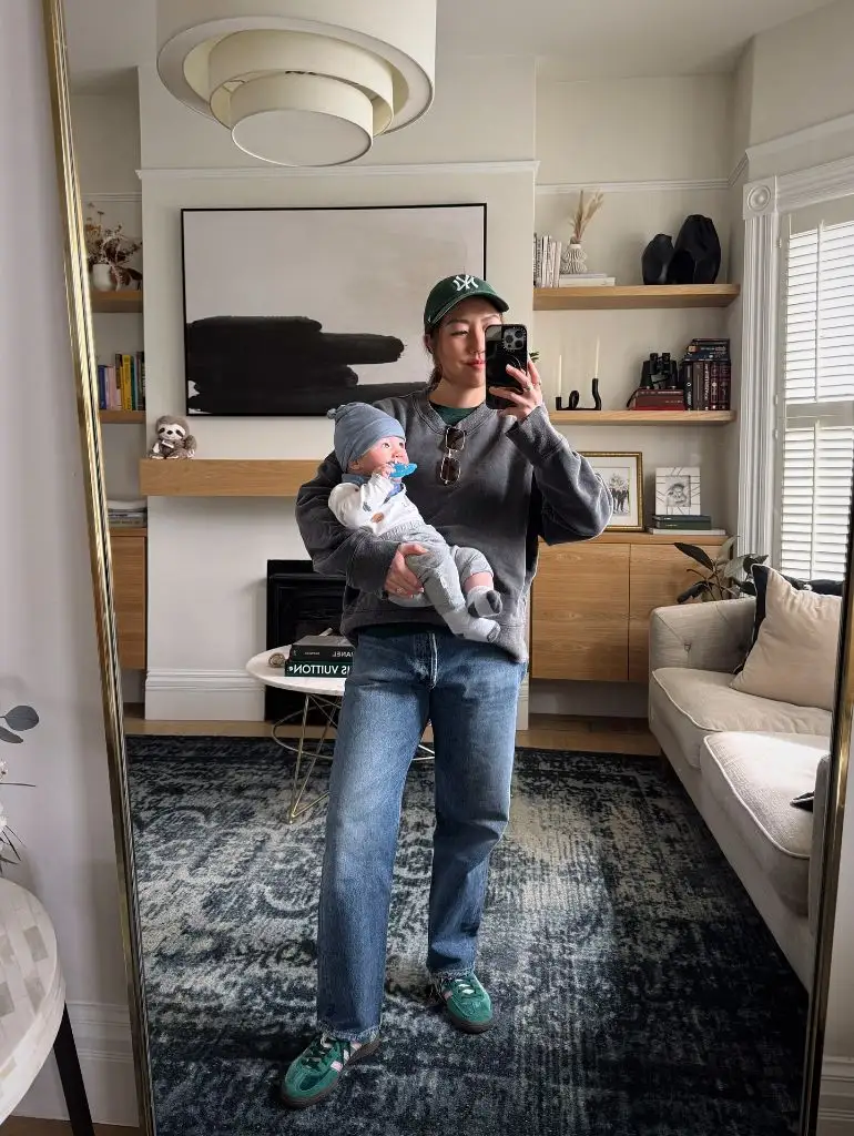 Mirror selfie with baby in grey sweatshirt and jeans with green cap