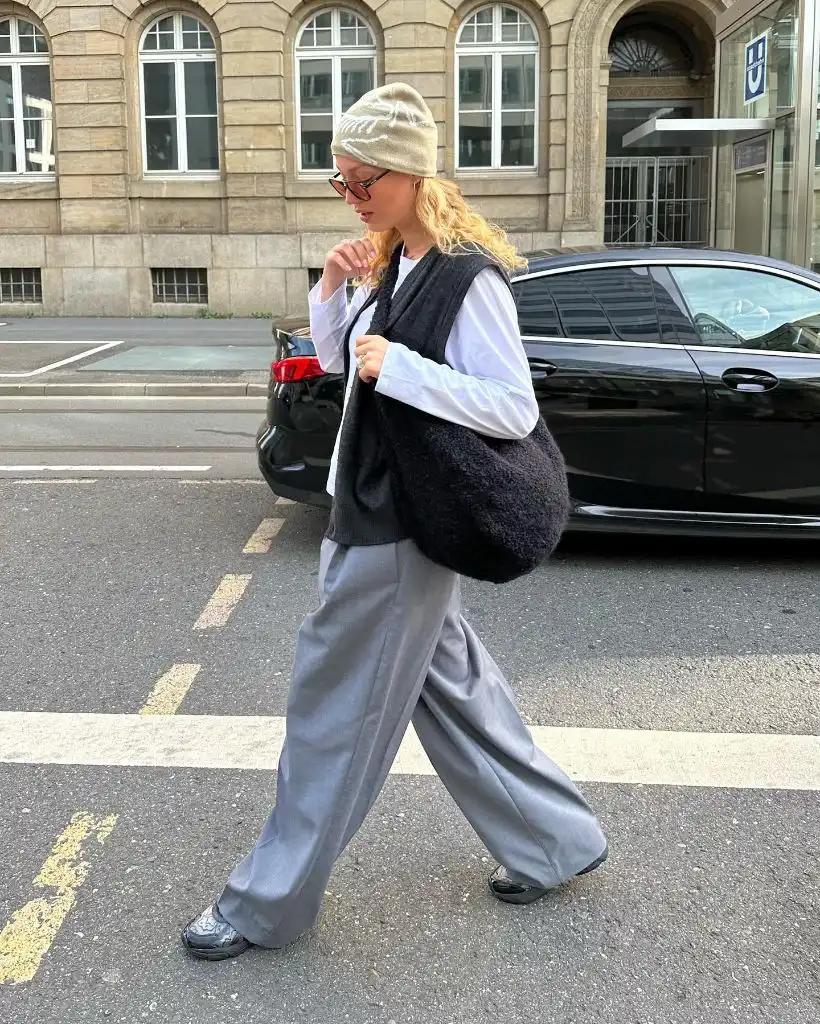 Beige beanie, white button-down shirt, black knit vest, grey wide-leg trousers, and dark sneakers