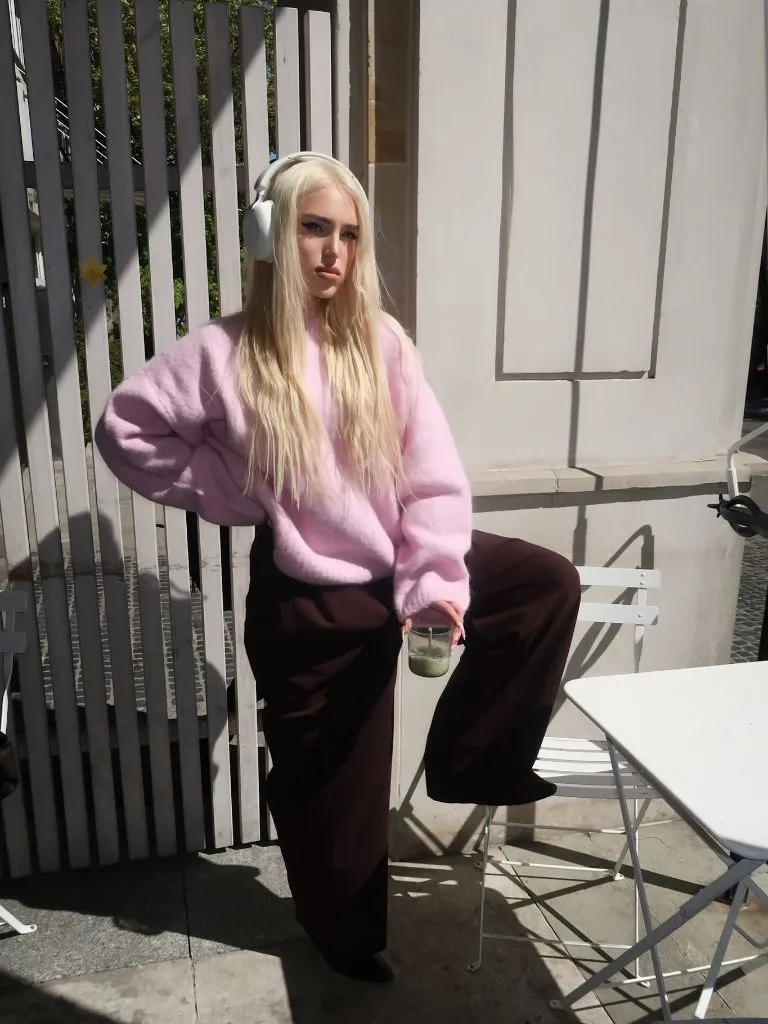 Pink mohair sweater with burgundy wide-leg trousers and white headphones at an outdoor cafe