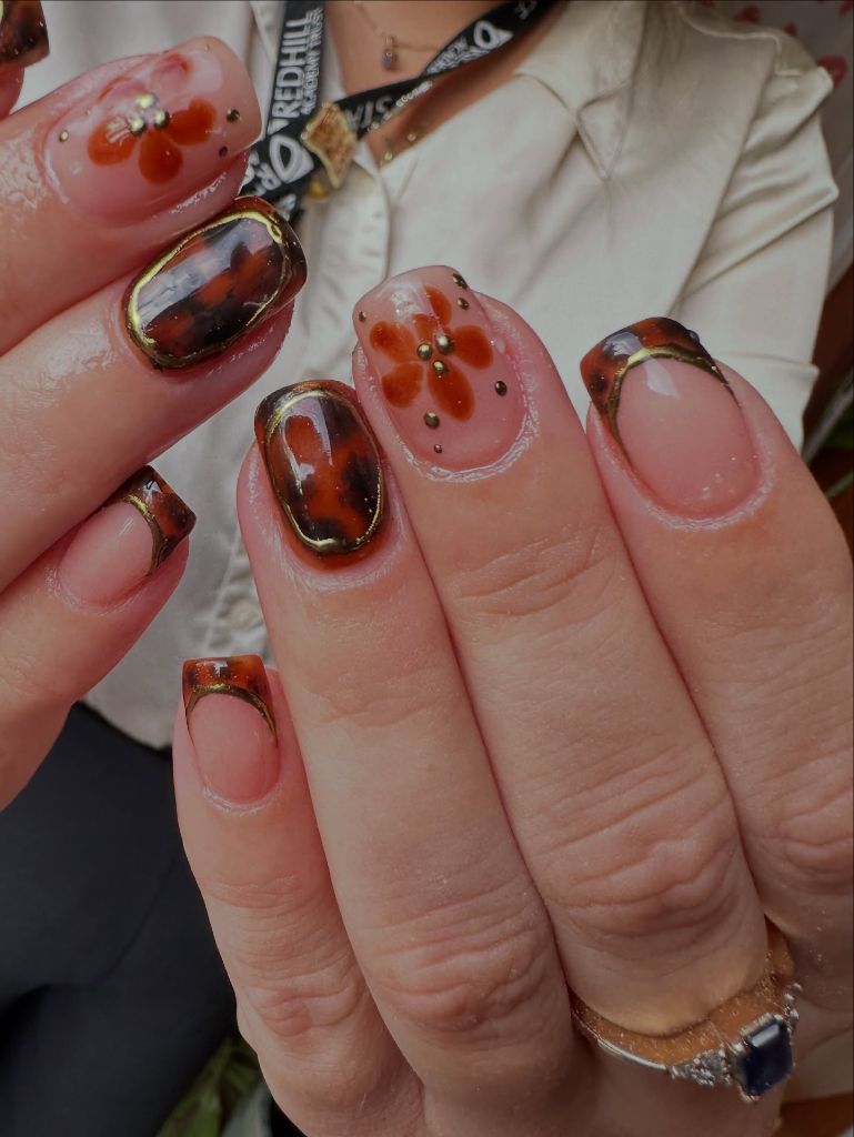 Tortoiseshell French tips with rust flower accents and gold details, August nail art 2026
