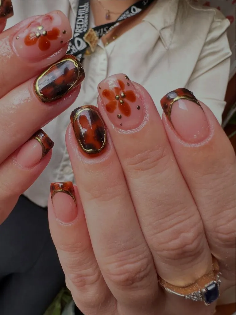 Tortoiseshell French tips with rust flower accents and gold details, August nail art 2026