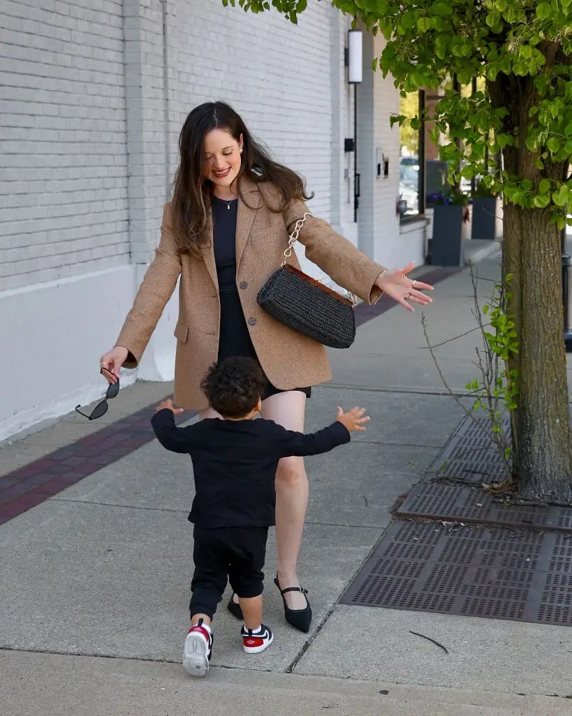 Mom on sidewalk with toddler wearing camel blazer over black