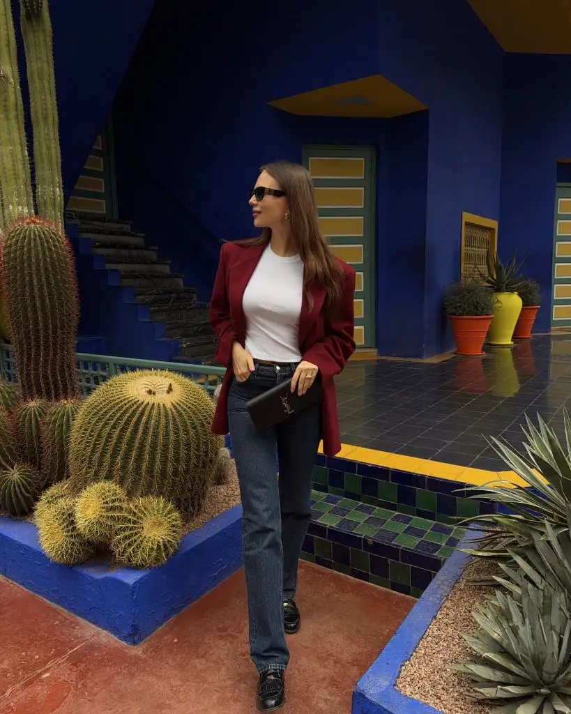 Burgundy blazer with white tee, dark denim jeans, and YSL clutch at Jardin Majorelle in Marrakech