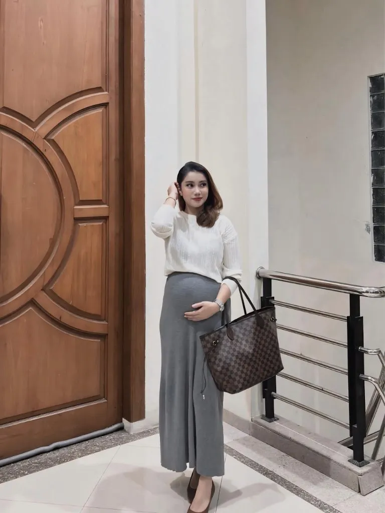 Pregnancy outfit with white sweater, gray wide-leg midi skirt, flats, and Louis Vuitton Neverfull tote