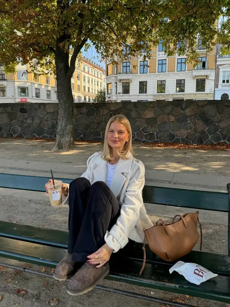 Cream boucle jacket with black trousers and brown suede boots on a park bench