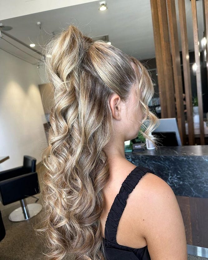 High voluminous ponytail with soft curls on long balayage hair, styled in a salon