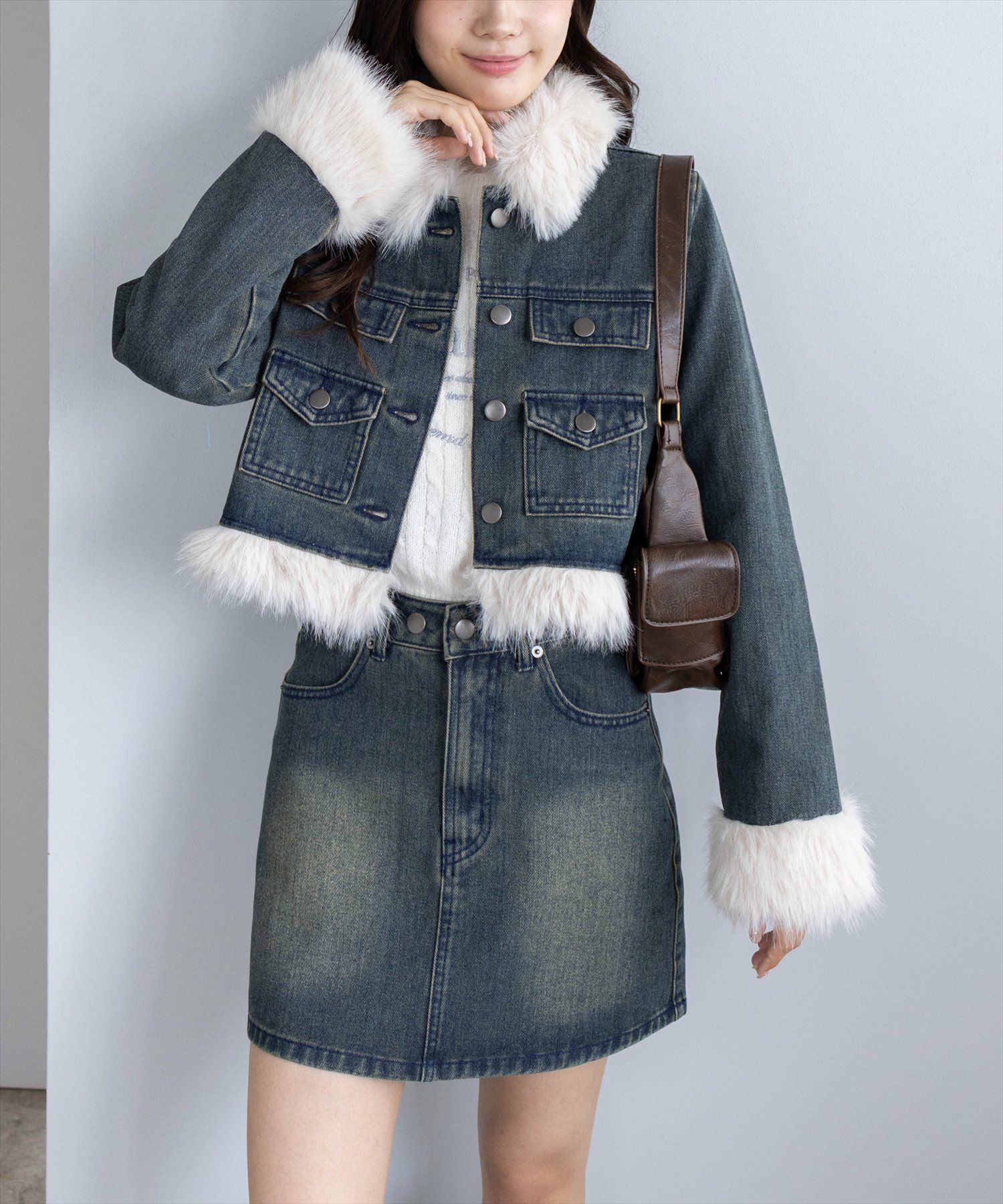 Woman wearing a cropped dark denim jacket with white faux-fur trim and a dark denim mini skirt