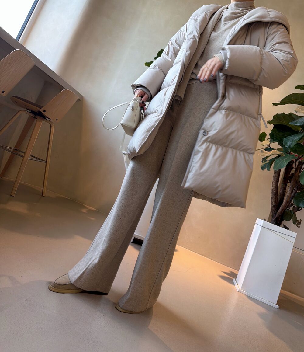 Woman in a cream puffer coat over a beige knit turtleneck and wide-leg knit trousers with a white mini bag