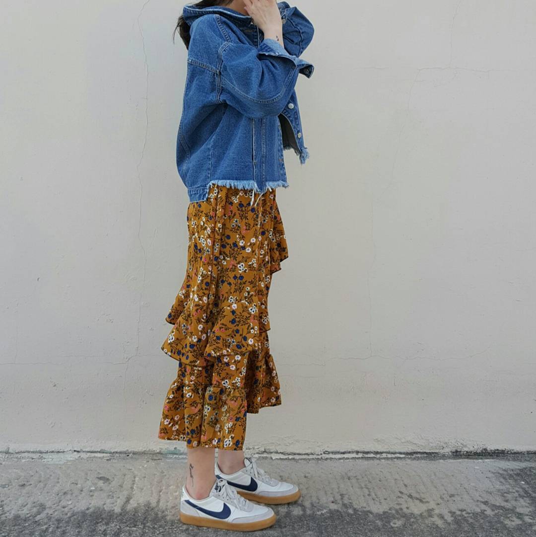 Woman in a mustard floral tiered midi skirt with a cropped frayed denim jacket and white and navy sneakers