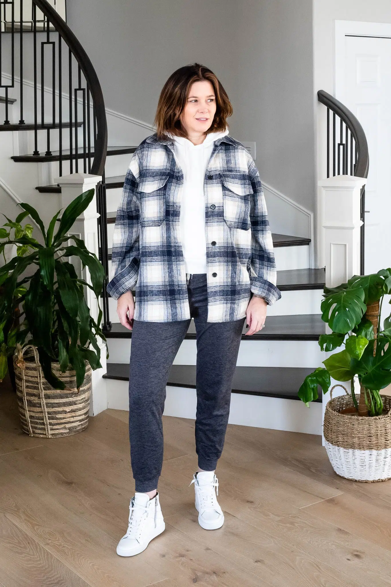 Woman in a navy plaid shacket over a white hoodie with charcoal joggers and white sneakers