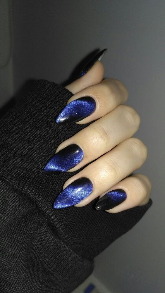 Stiletto nails in black velvet cat-eye with luminous blue magnetic shimmer streaks; real photography.