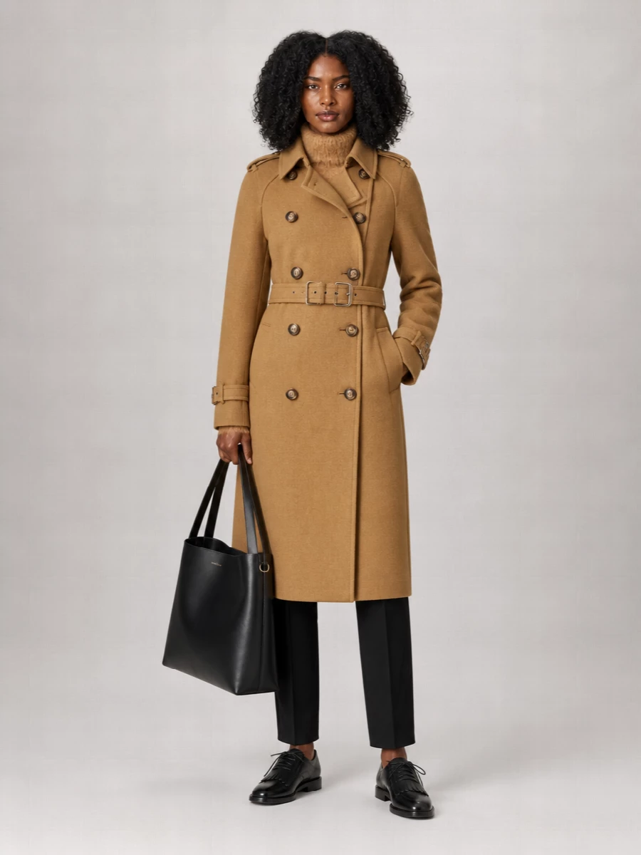 A camel double-breasted belted long coat over black cropped trousers, black oxfords and a black tote.