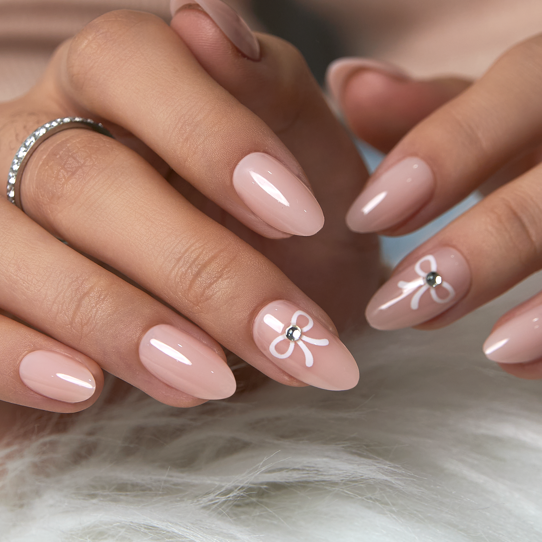 Nude almond nails with hand-painted white bows and tiny crystal centers