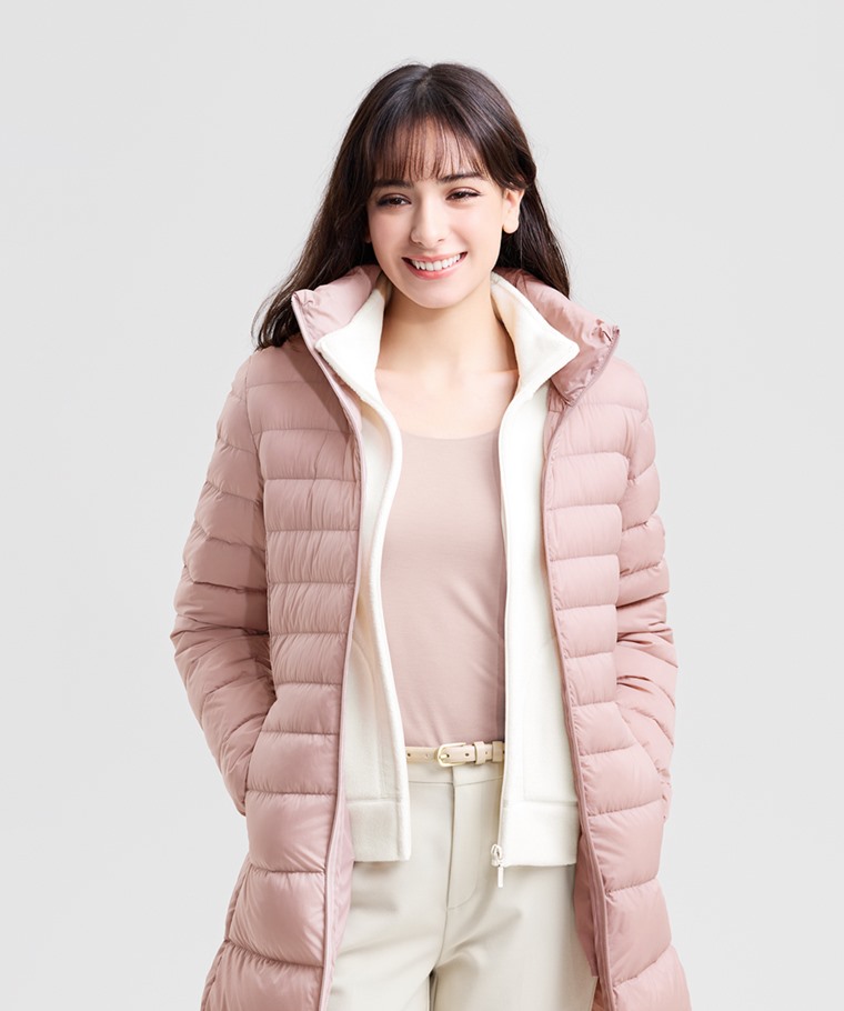 A woman wearing a blush pink long puffer coat with cream layers