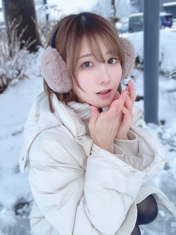 Woman wearing blush pink earmuffs and a white puffer jacket in the snow