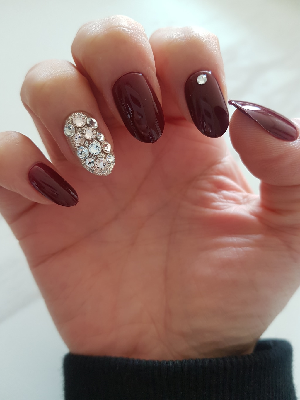 Burgundy oval nails with one nail fully covered in rhinestones and a single crystal accent on another