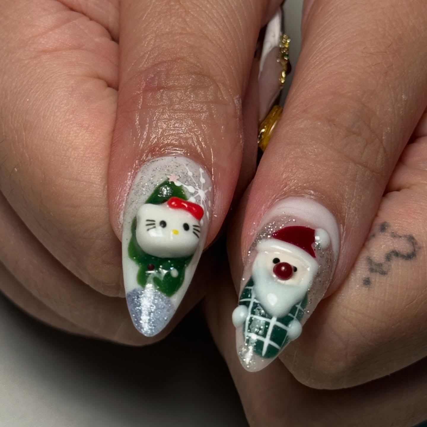 Long almond nails with a 3D Hello Kitty face on a green Christmas tree, a 3D Santa face on green plaid and silver glitter