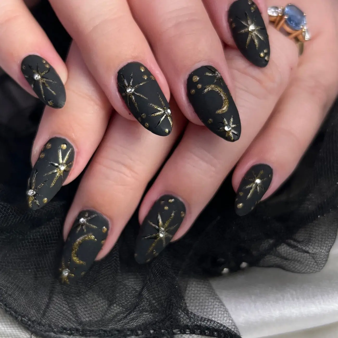 Matte black almond nails with hand-painted gold moon and starburst art