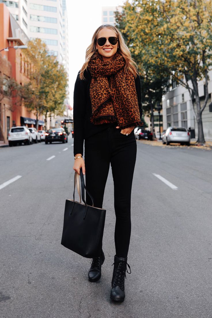 Woman in a rust leopard print scarf with an all-black outfit and lace-up boots on a city street