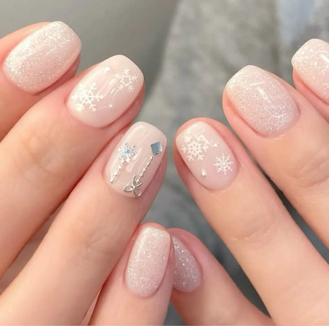 Short sheer nude Christmas nails with white snowflakes and silver charm chains