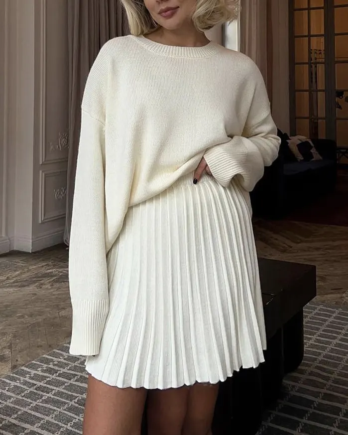 Oversized ivory knit sweater tucked into a white pleated knit mini skirt