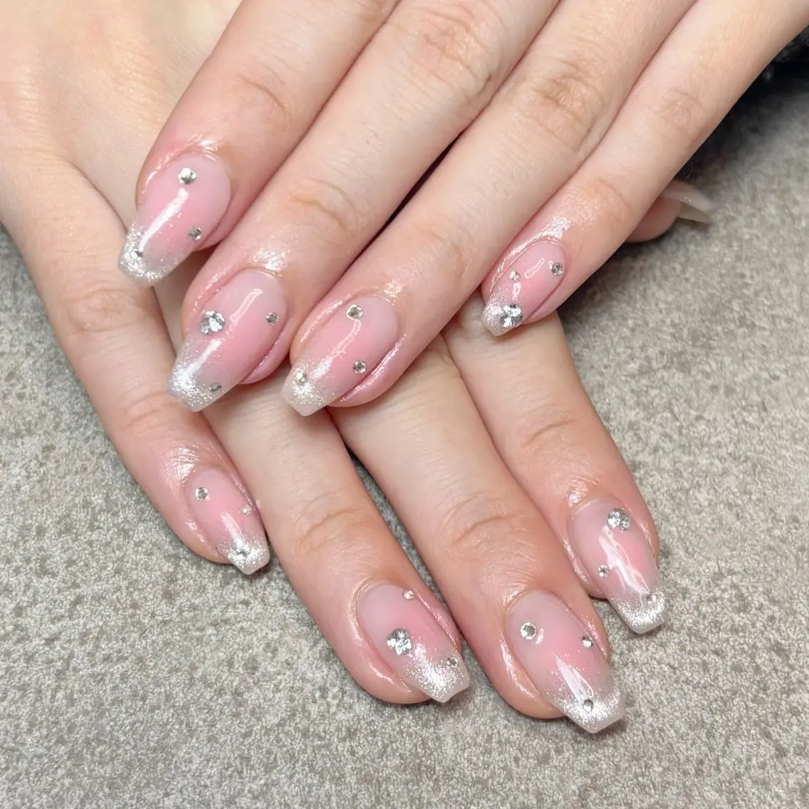 Medium almond nails in sheer pink with silver glitter tips and scattered clear rhinestones