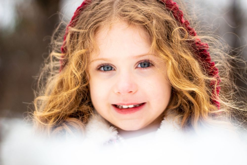 Little girl with curly red hair wearing a red knit headband in a snowy winter setting