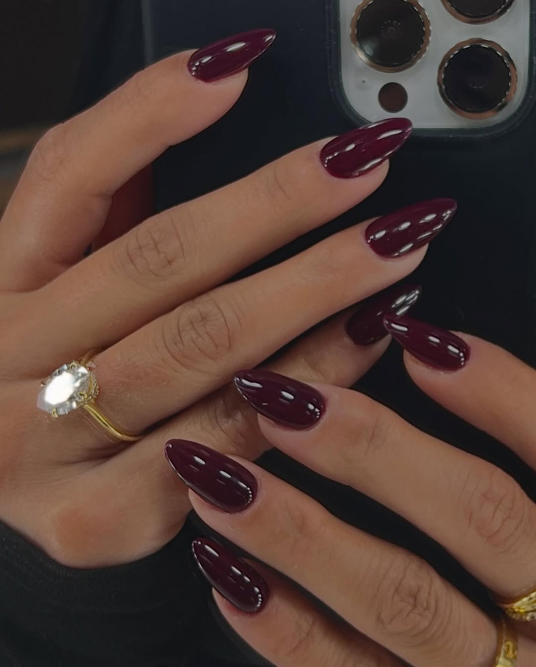 Glossy burgundy almond nails in a mirror selfie