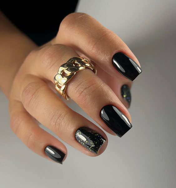Short square black nails with a gold and green micro-glitter accent nail and gold ring
