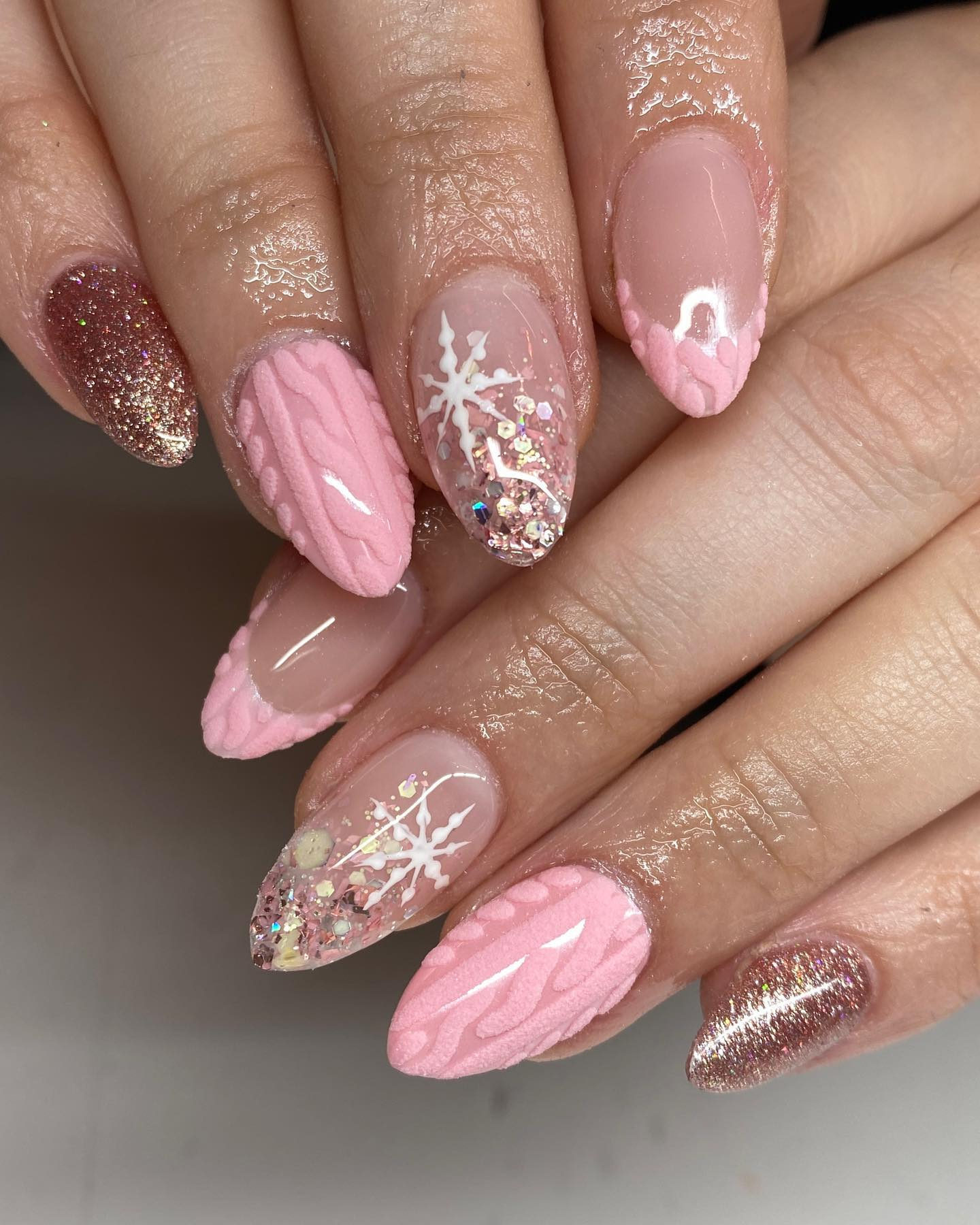 Medium almond nails in blush pink with cable-knit sweater texture, snowflakes and glitter accents