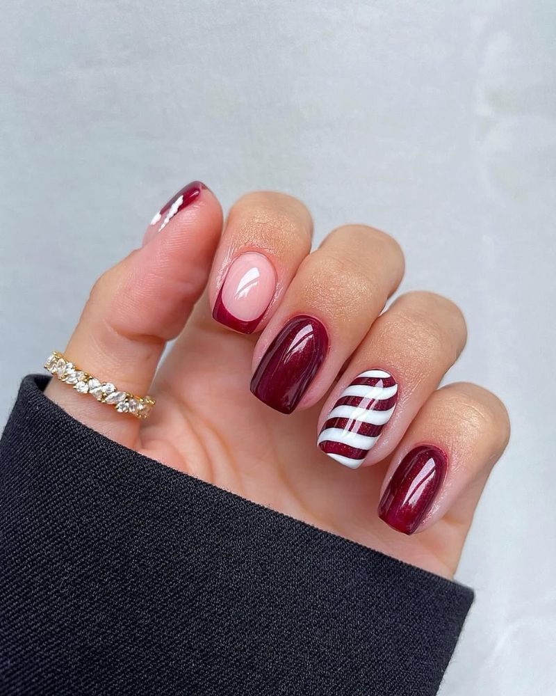 Burgundy nails with one red and white candy cane striped accent nail