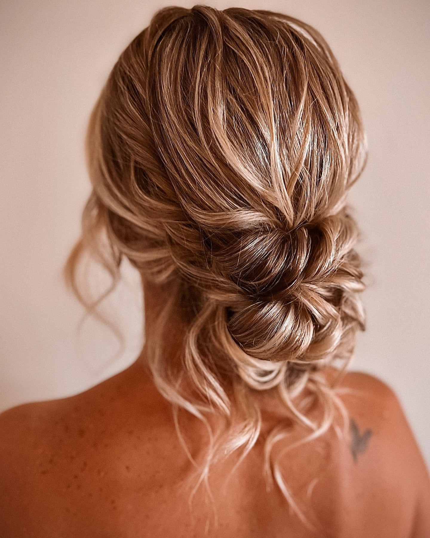 Low messy bun with pulled-out curled tendrils on blonde hair, back view