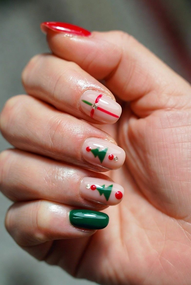 Nude nails with tiny green Christmas tree nail art, red dots, and solid red and green accent nails