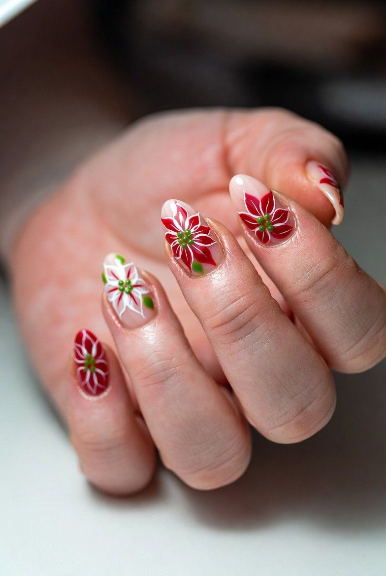 Almond nails with hand-painted red and white poinsettia flowers and green leaves on sheer nude