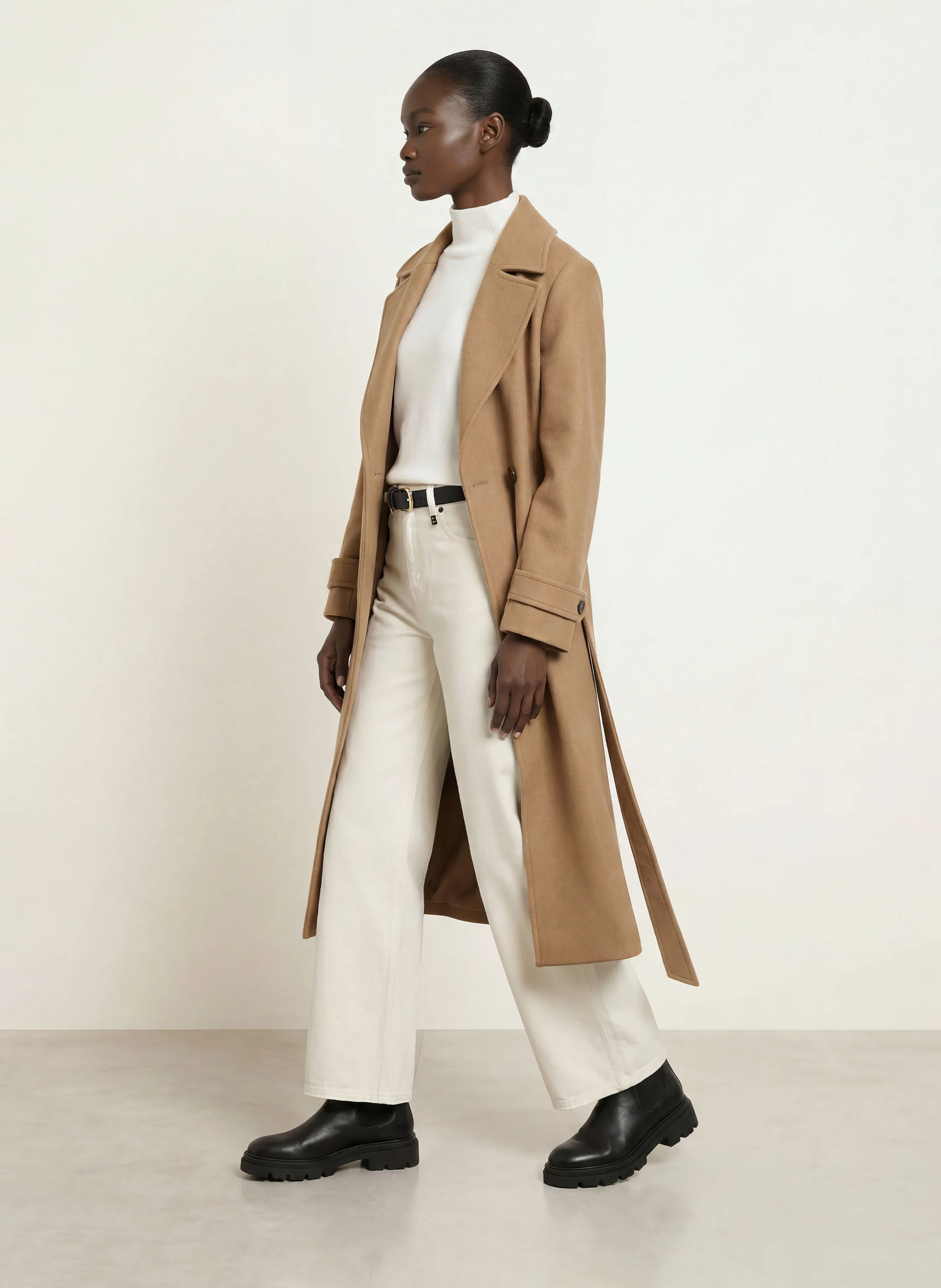 Woman in a camel coat, white turtleneck, white jeans and black lug-sole Chelsea boots