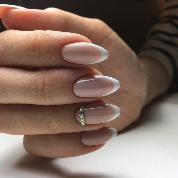 Almond nails with soft pink nude French tips and a crystal band on the ring finger