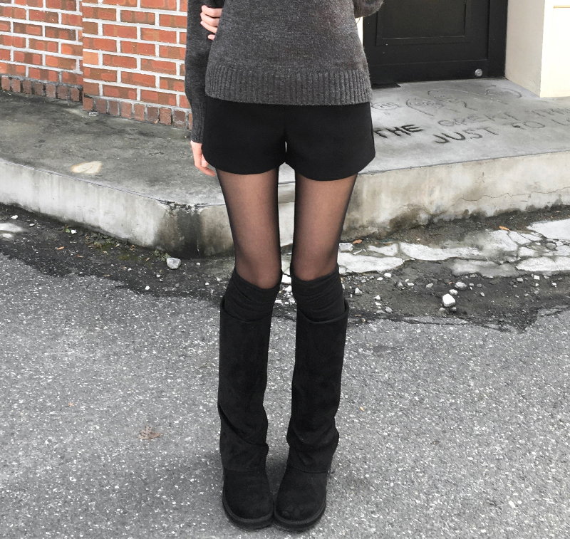 Woman in black flat slouchy boots with black shorts, tights and a grey sweater