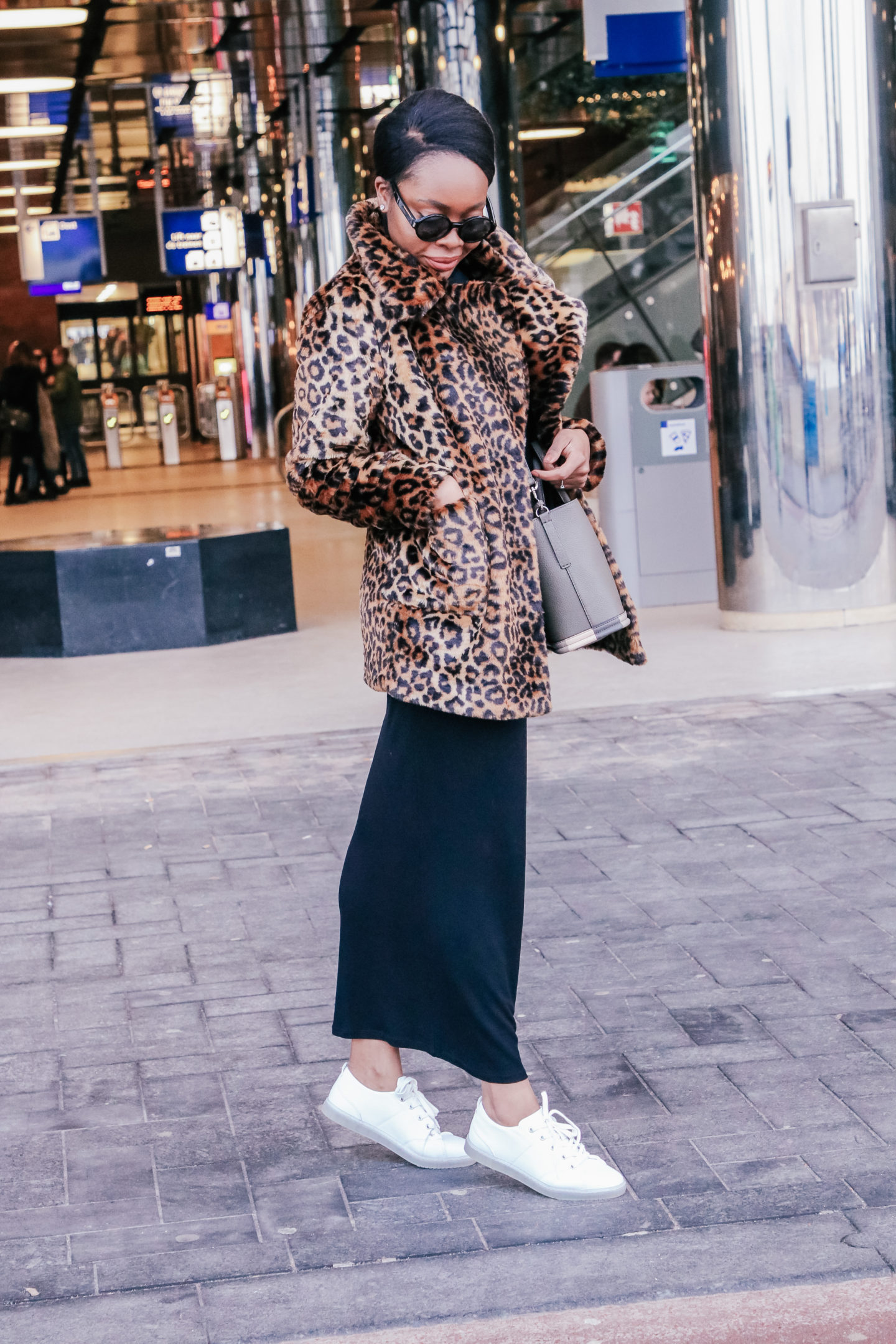 Woman in a leopard print coat with a black knit midi skirt and white sneakers