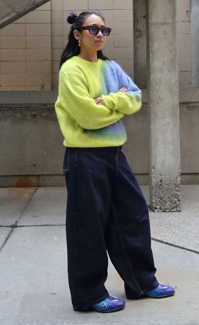 Woman in a lime-green to blue fuzzy ombre sweater with dark wide-leg jeans and metallic purple sneakers